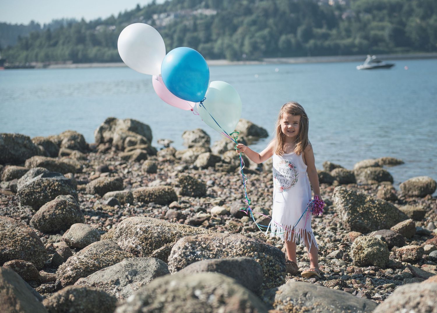 White dress and colorful balloons create celebratory scene against mountain lake backdrop.