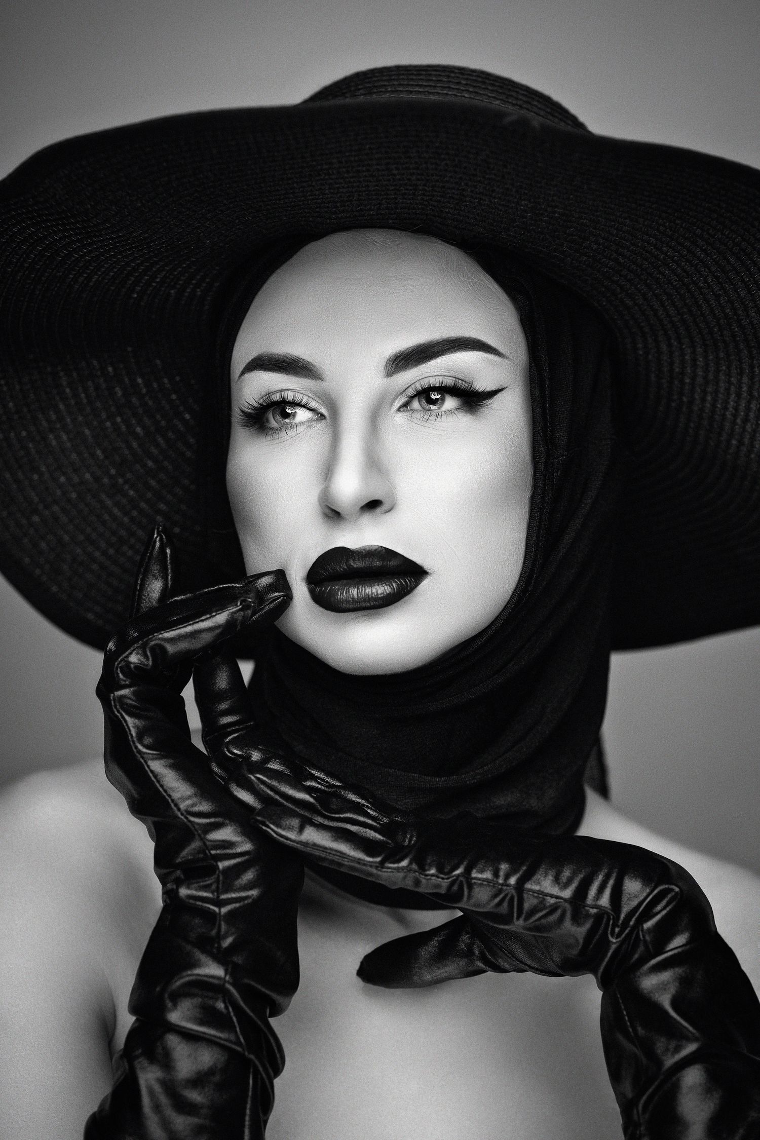 Dramatic black and white portrait featuring a wide brim hat, dark lipstick, leather gloves and elegant vintage styling.