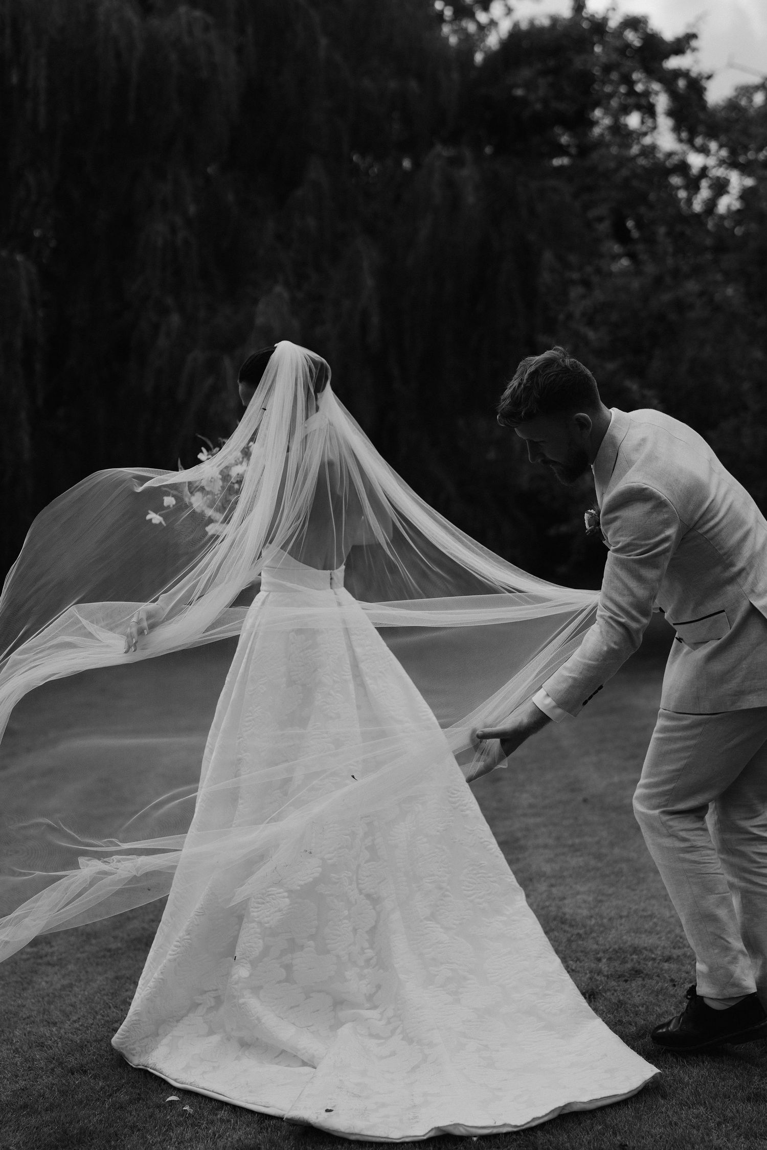 brides veil blowing in the wind as groom holds onto it in gardens in islip, Oxfordshire