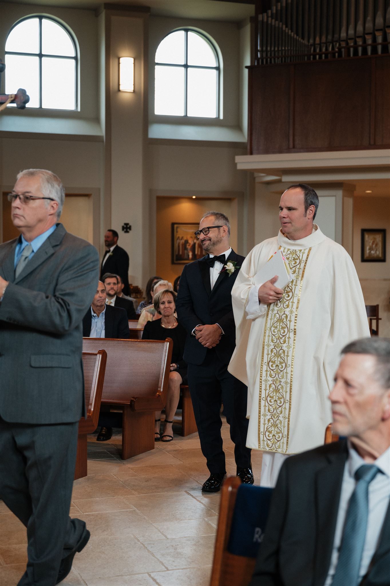 Church ceremony with clergy in white robes and guests seated in wooden pews.