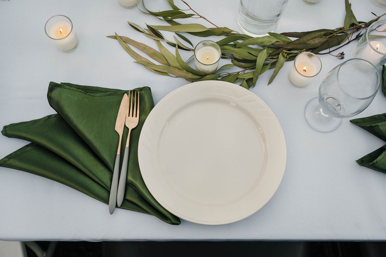 Place setting with white plate, green napkin, and tealight candle on crisp white tablecloth.