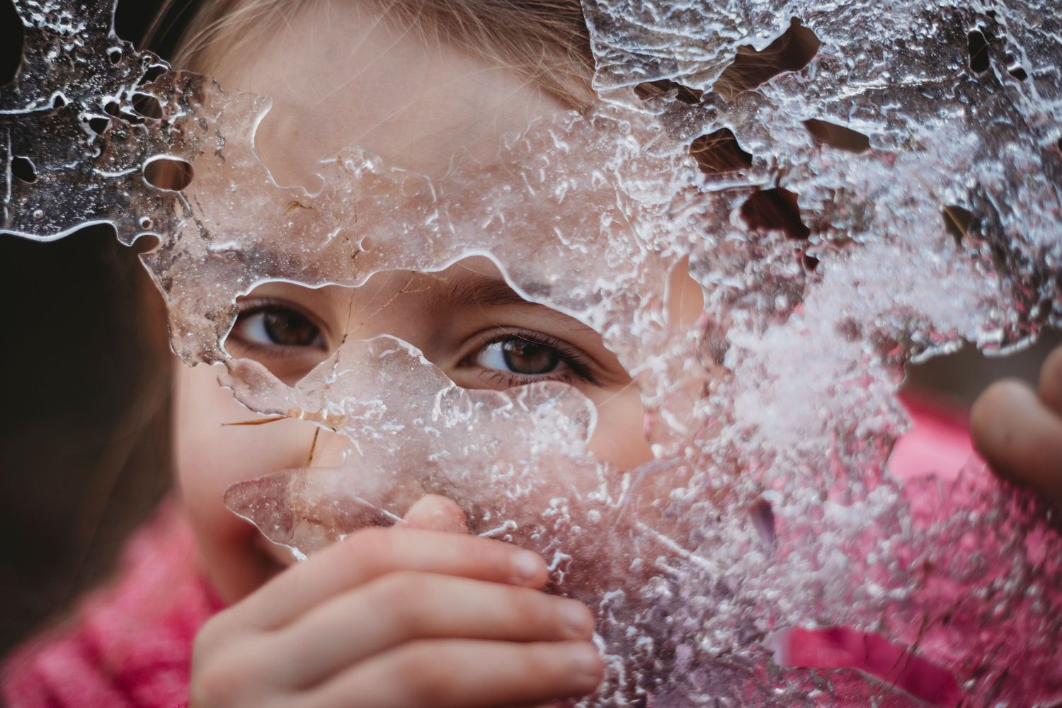 Looking through shattered ice with a pink winter coat visible in the background.