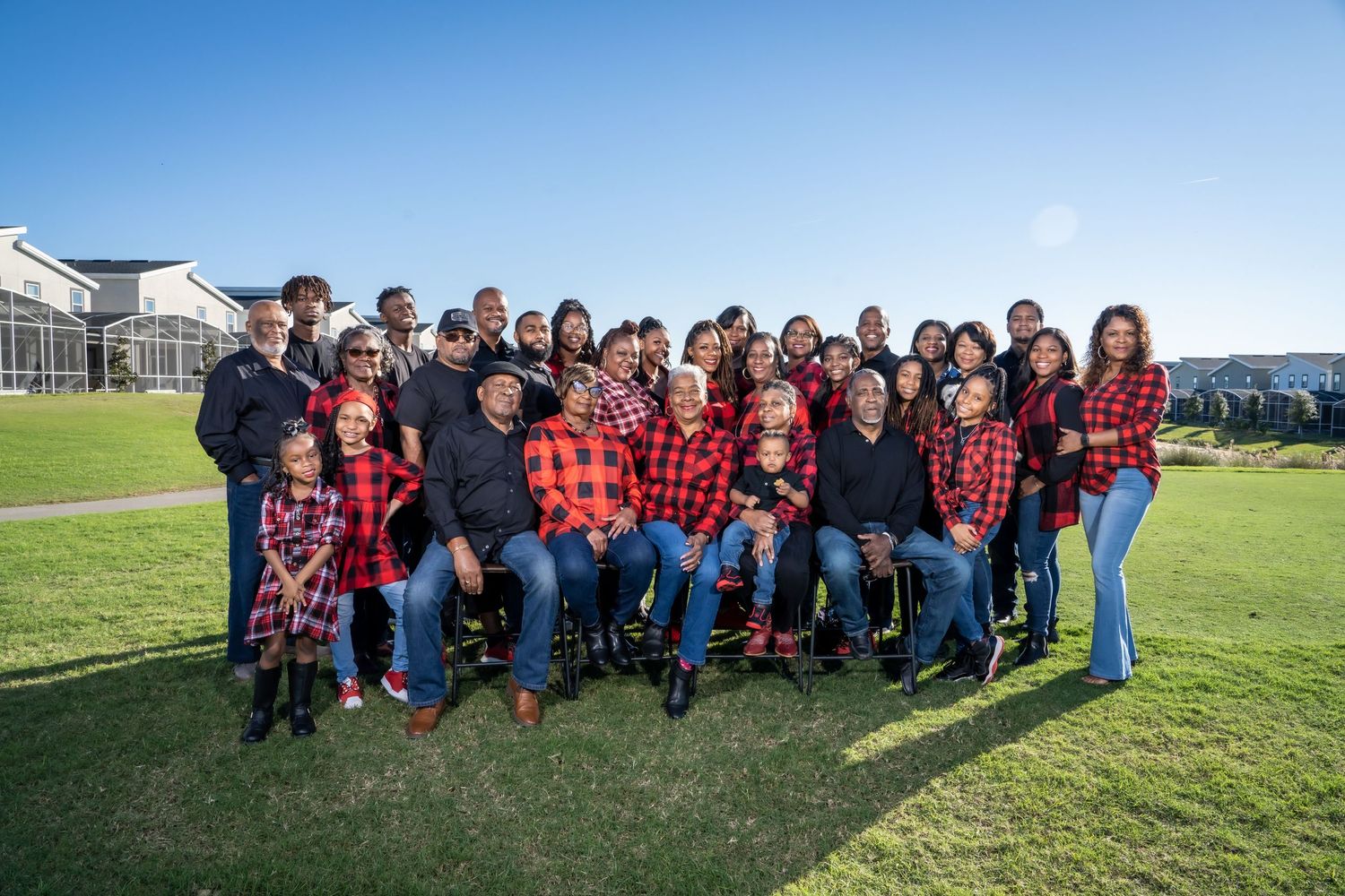 Large group wearing coordinated red plaid shirts poses together on grass field.