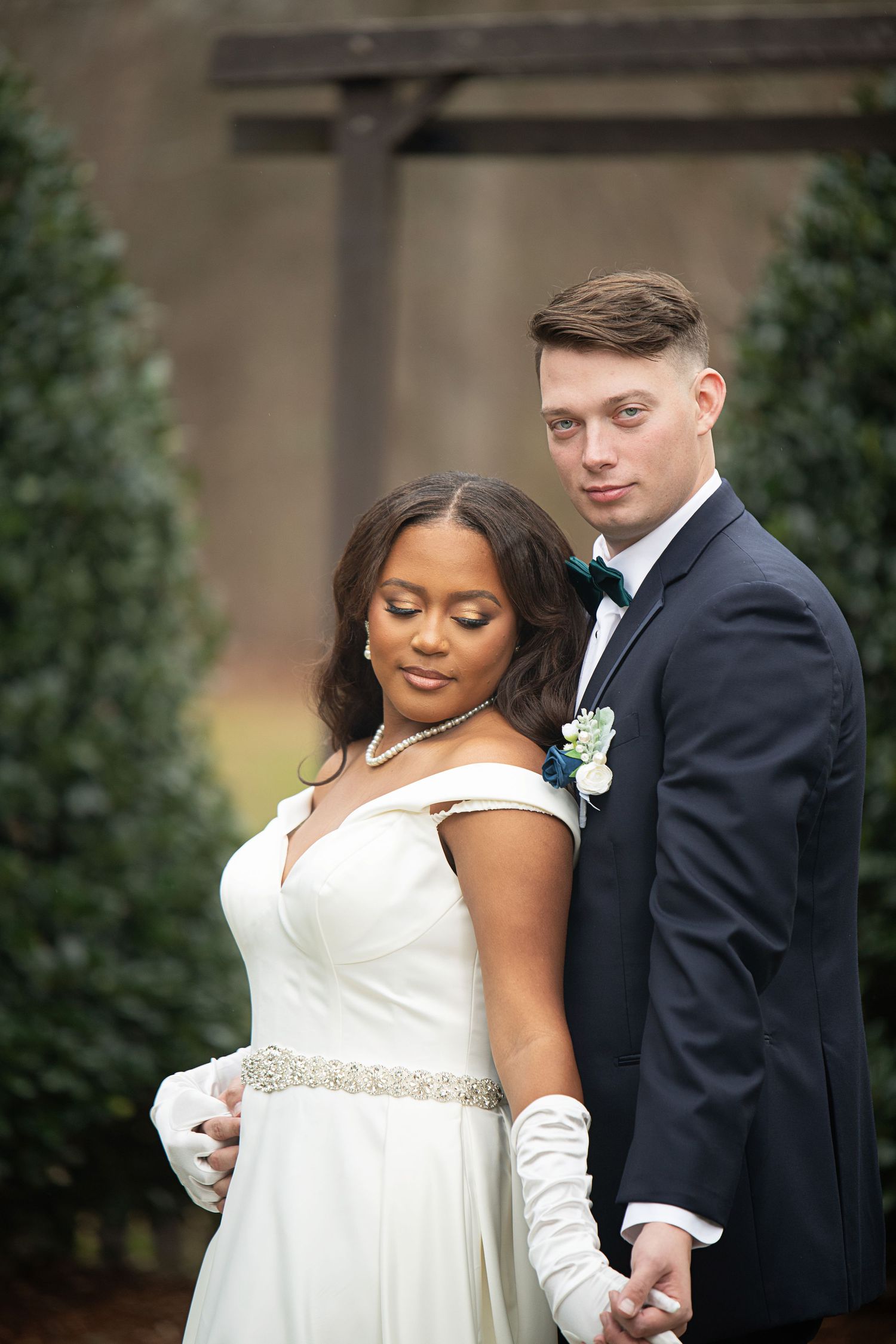 An elegant wedding portrait featuring the couple in formal attire against decorative topiaries.