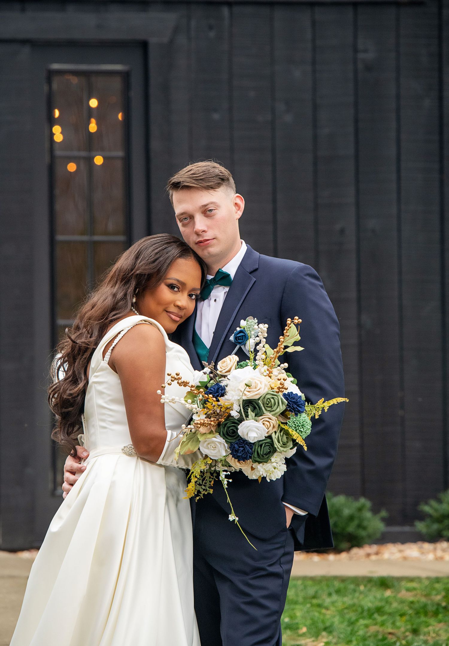 A romantic wedding portrait against a dark wall with twinkling lights in the background.