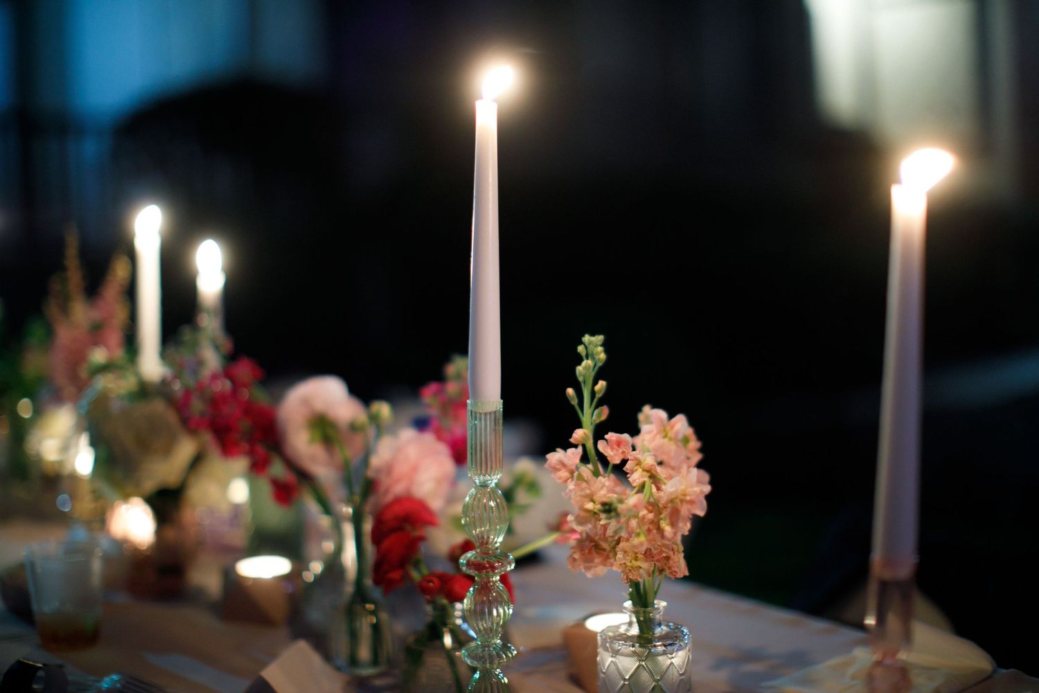 Elegant table setting with lit candles and delicate floral arrangements in small vases.