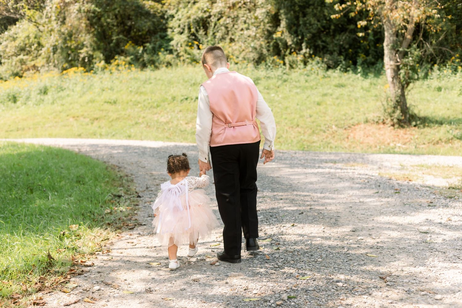 Couple walking hand in hand down a scenic path surrounded by grass and trees.