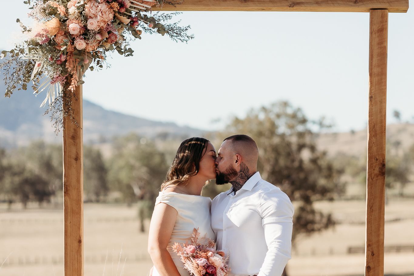 Romantic outdoor wedding photos under a wooden arch decorated with peach floral arrangements.