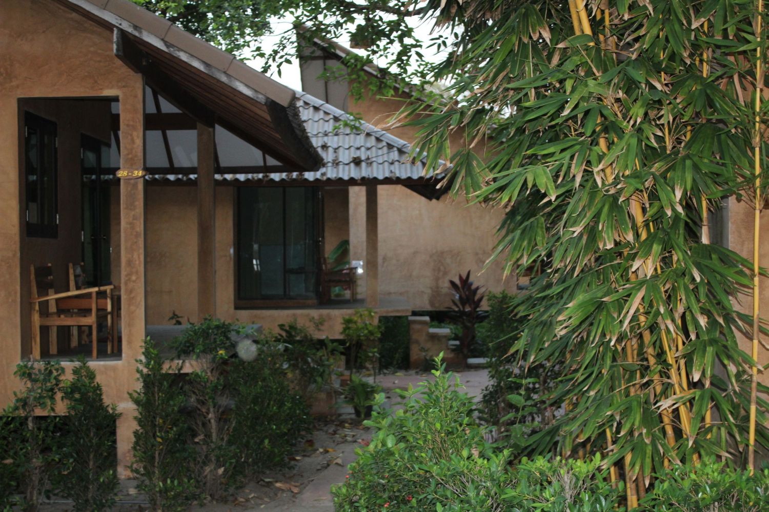 Small house with sloped awning features lush green bamboo and shrubs in the front garden.
