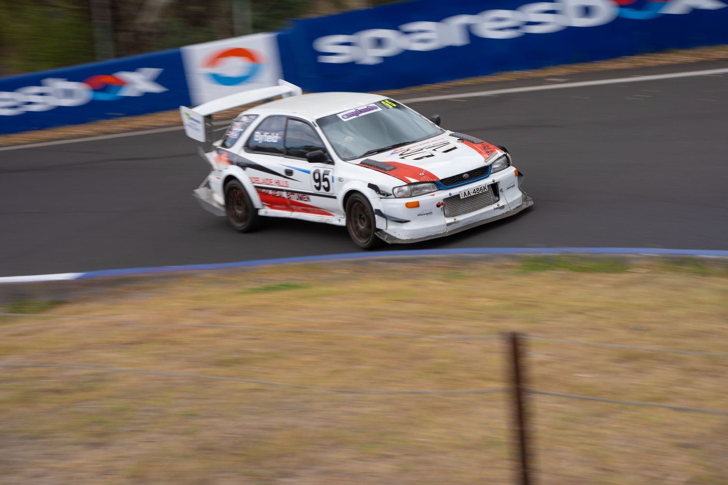 White rally car racing at high speed on a curved racetrack.