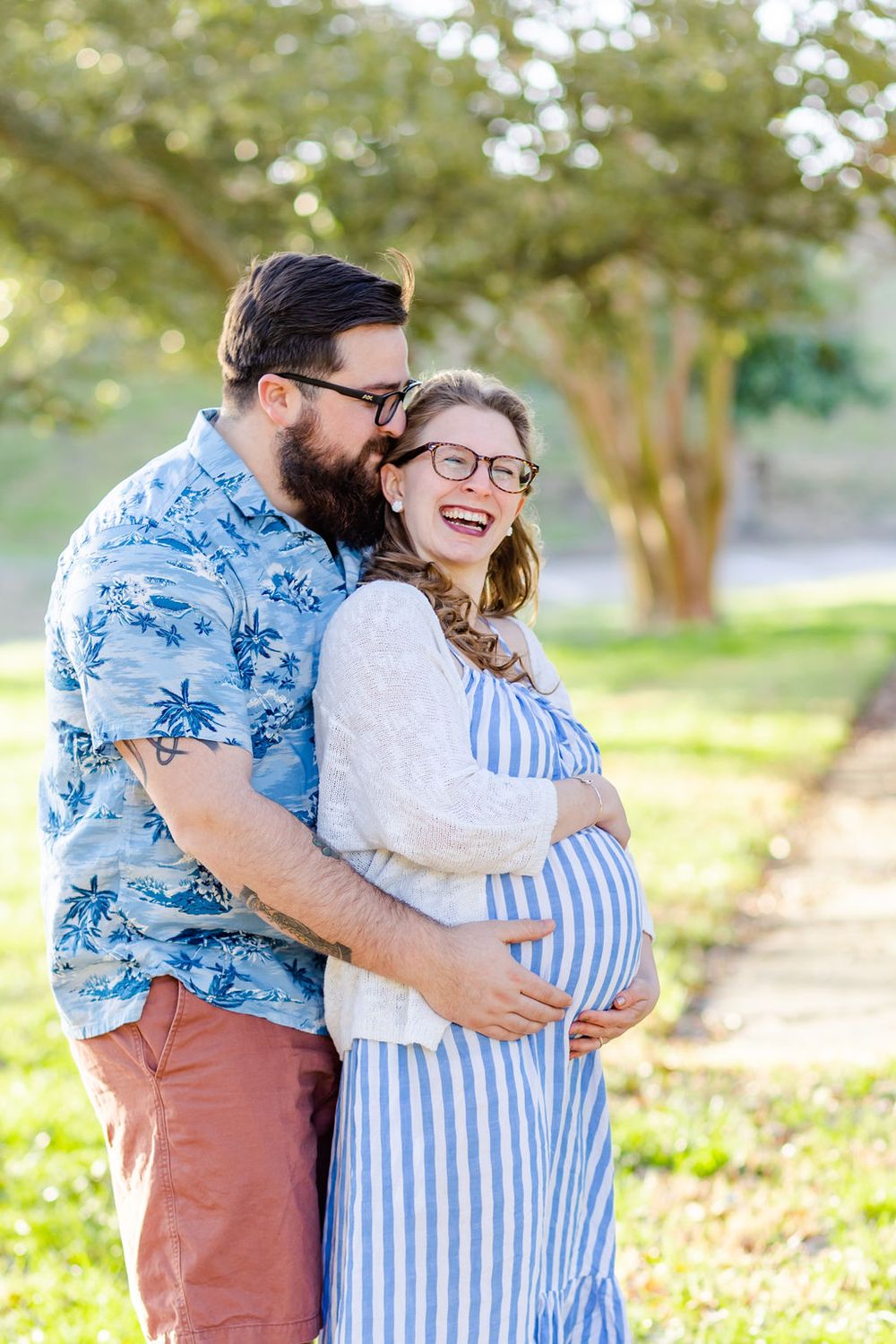 Joyful expecting couple embracing outdoors in casual spring attire.