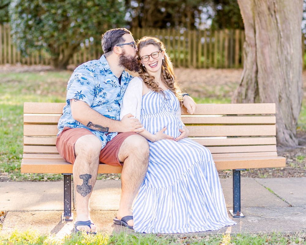 Couple sharing tender moment on park bench wearing blue Hawaiian shirt and striped dress.