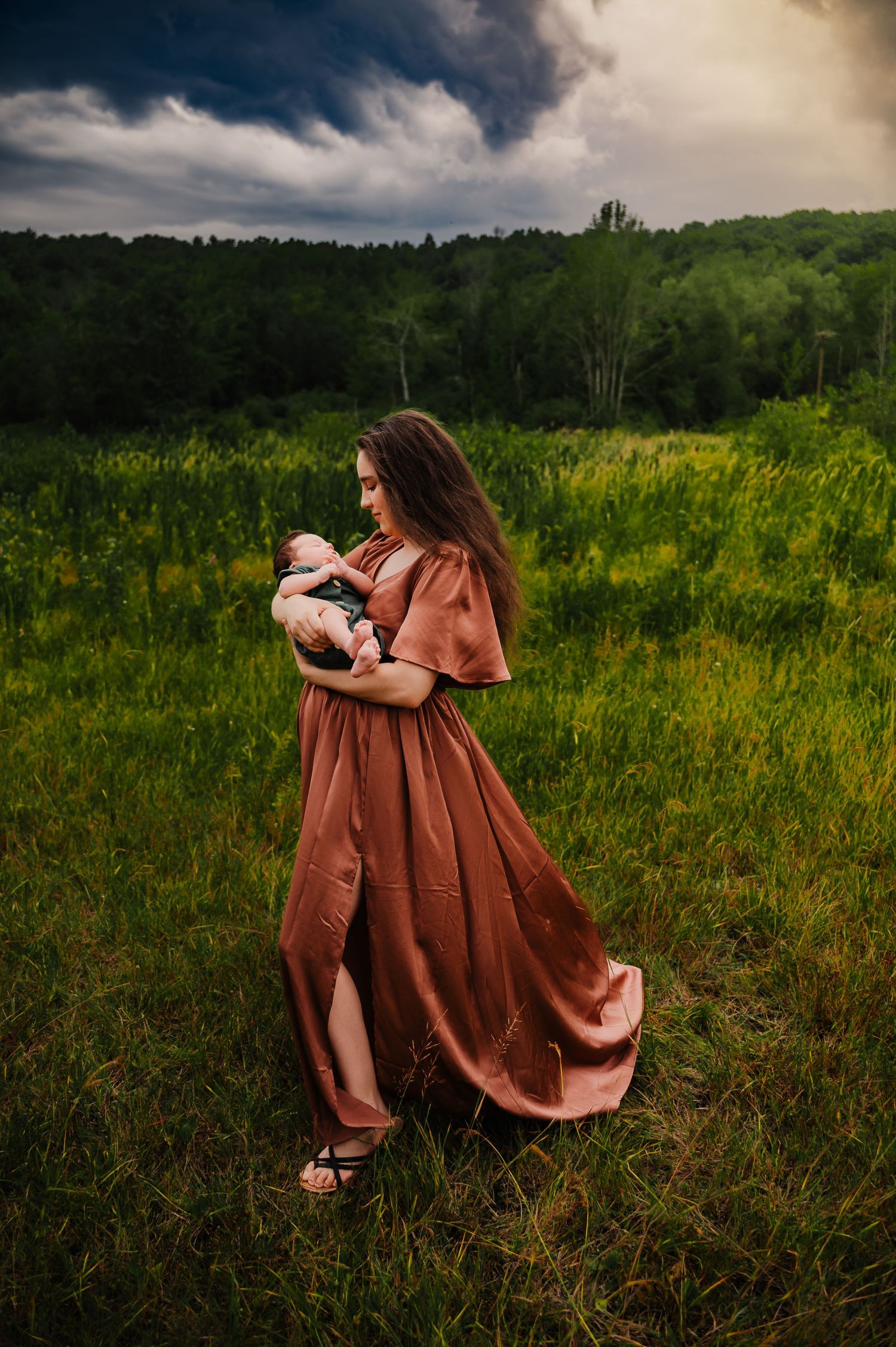 women wearing flowing rose colored gown holding baby in field in Staten Island, NY