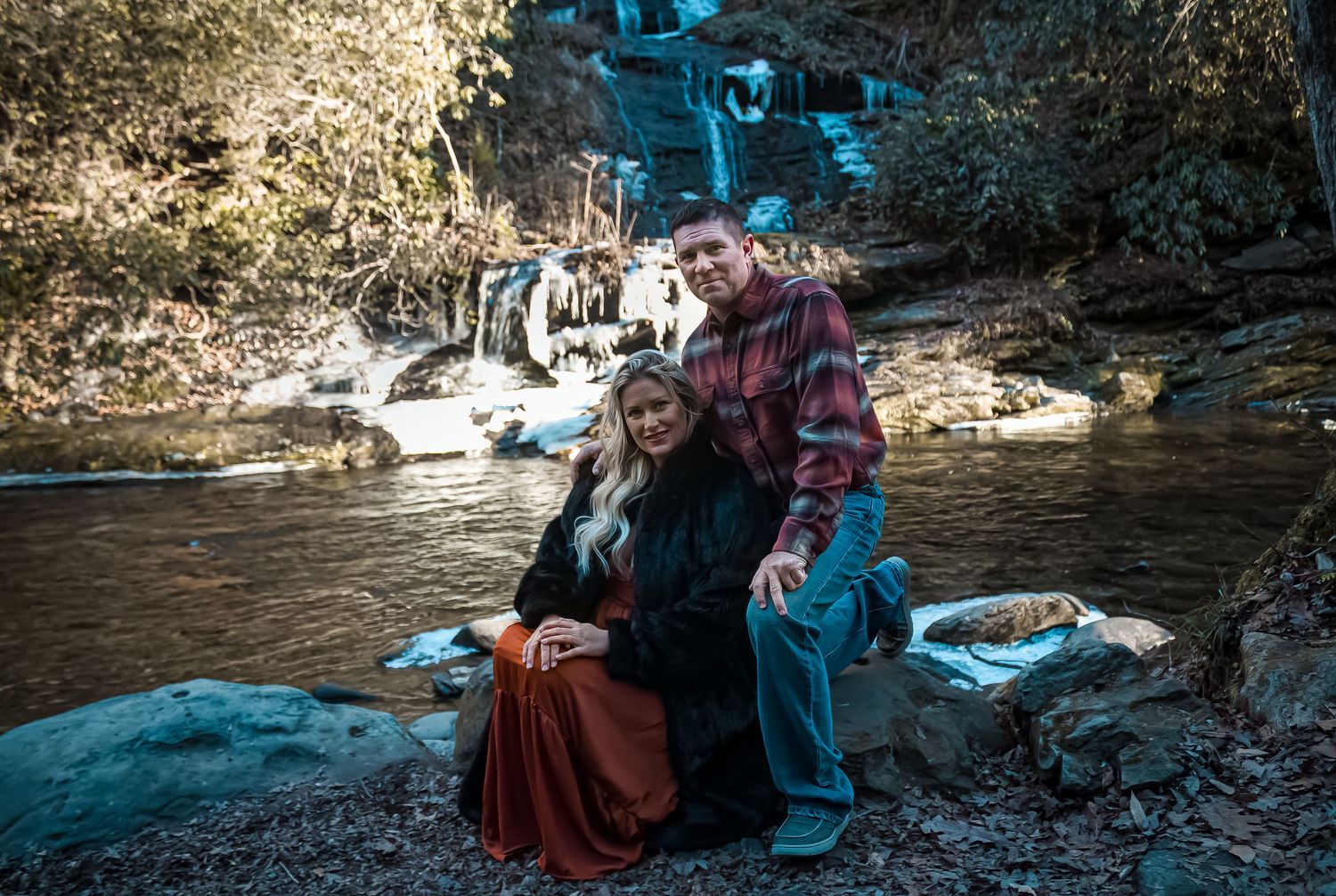 People sitting on rocks by a scenic waterfall in a forest setting during golden hour.