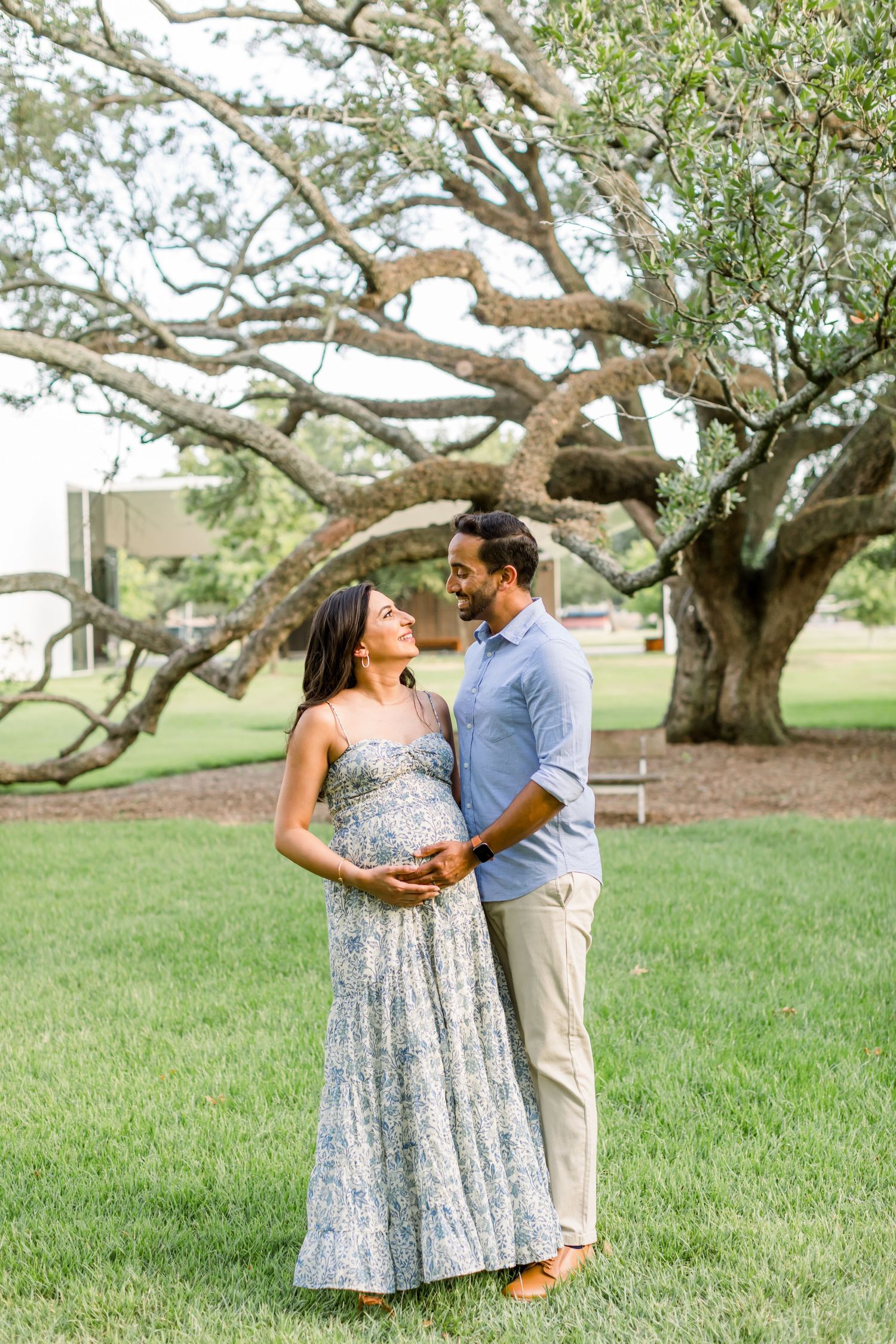 Couple poses beneath twisted branches of an ancient oak tree during pregnancy photoshoot.