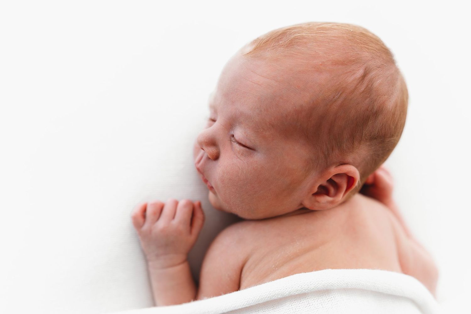 Side profile of sleeping newborn baby swaddled in white blanket.