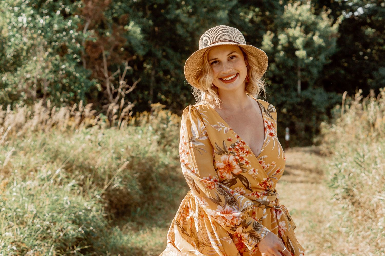 Woman in floral dress and sun hat walking through a lush garden setting.