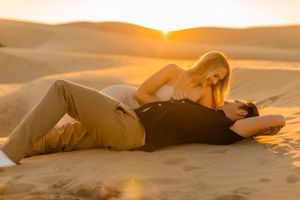 Couple lying together on sand dunes during sunset photoshoot.