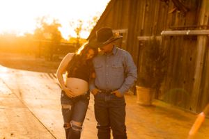 Couple standing together beside rustic barn in warm sunset light.