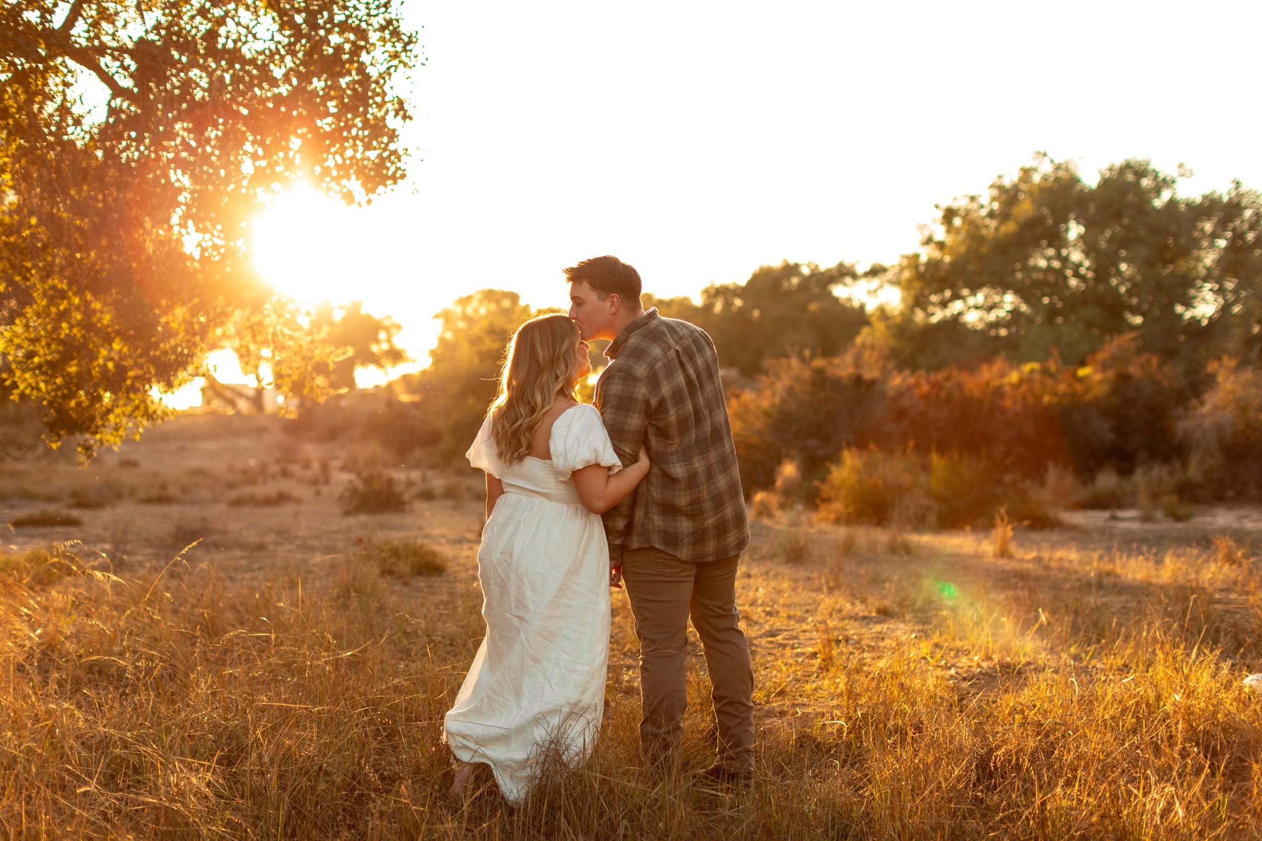 A couple shares an intimate moment in a golden field during sunset.