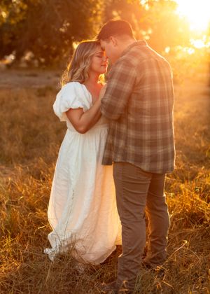 A romantic sunset engagement photo in a field with golden light filtering through trees.