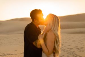 Silhouetted couple sharing intimate moment on desert dunes at sunset.