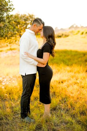 A romantic couple embraces in a golden field during sunset.