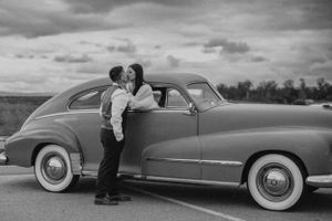 A vintage black and white photo of a couple by a classic car.