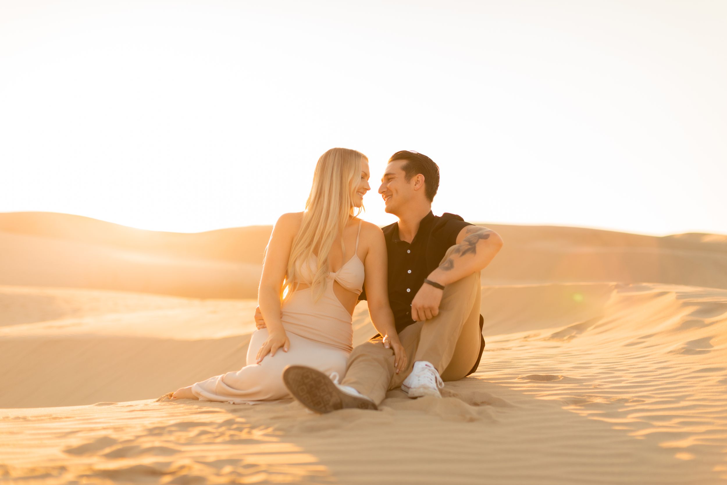 Couple sitting together on sand dunes during sunset.