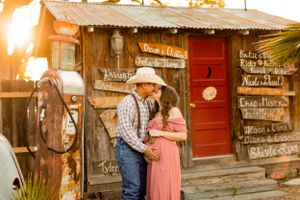 Couple embraces in front of rustic wooden building at sunset.