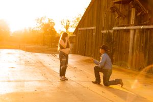 Romantic sunset proposal scene in front of rustic wooden barn.