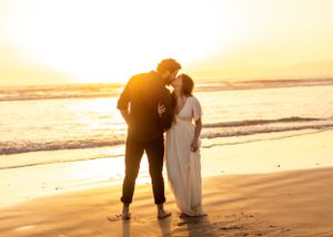 Silhouetted couple embracing on beach at golden sunset.