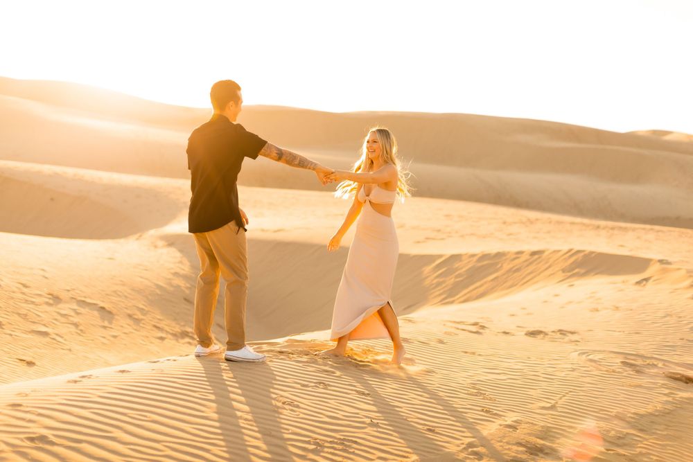 Couple holding hands while walking on sand dunes during golden hour.