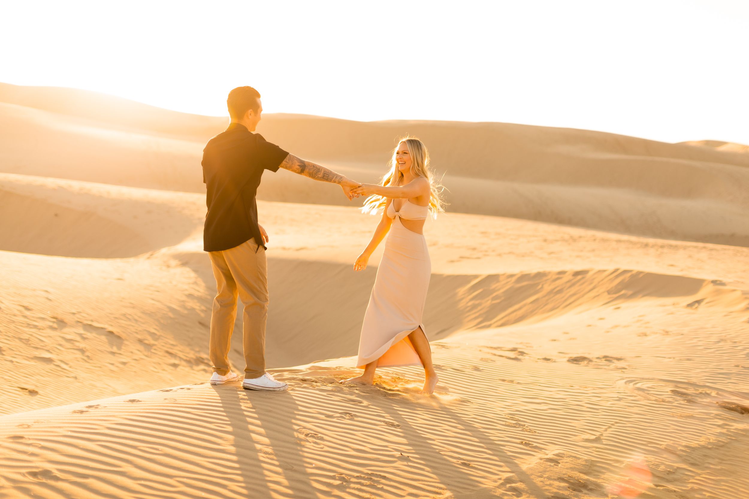 Couple holding hands while walking on sand dunes during golden hour.