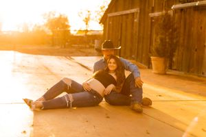 Couple relaxing together on ground near wooden barn during sunset.