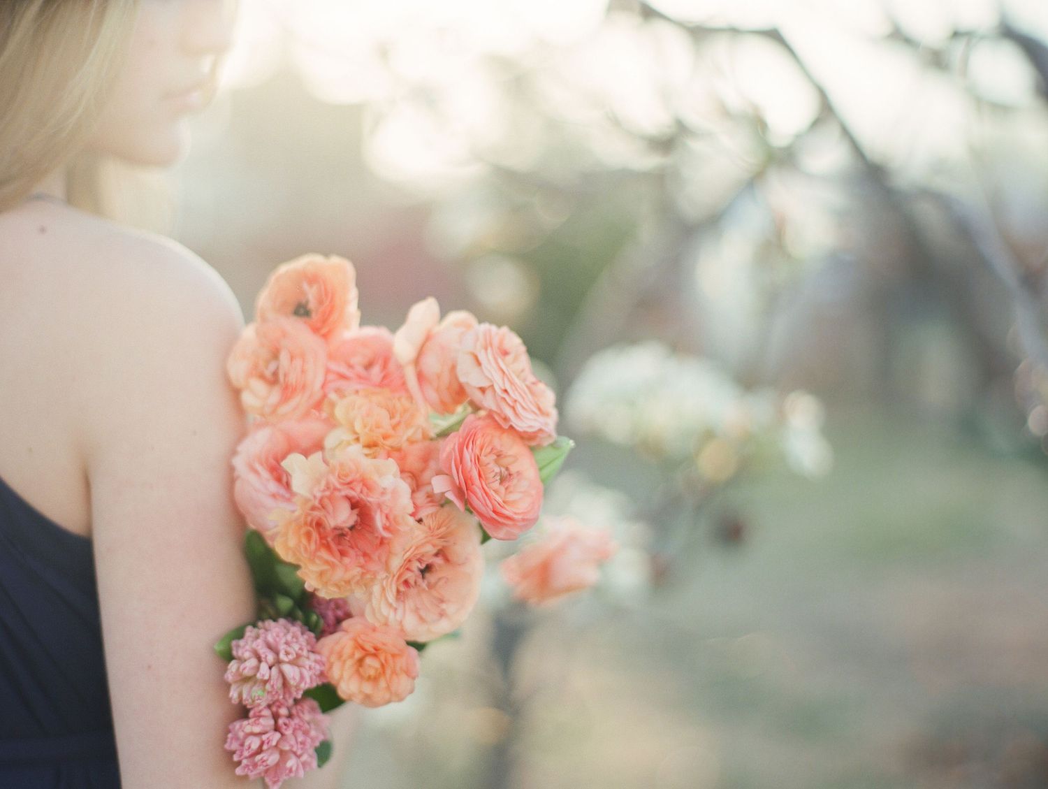 mostly soft focus of girls profile and shoulder holding apricot colored ranunculus in her arms