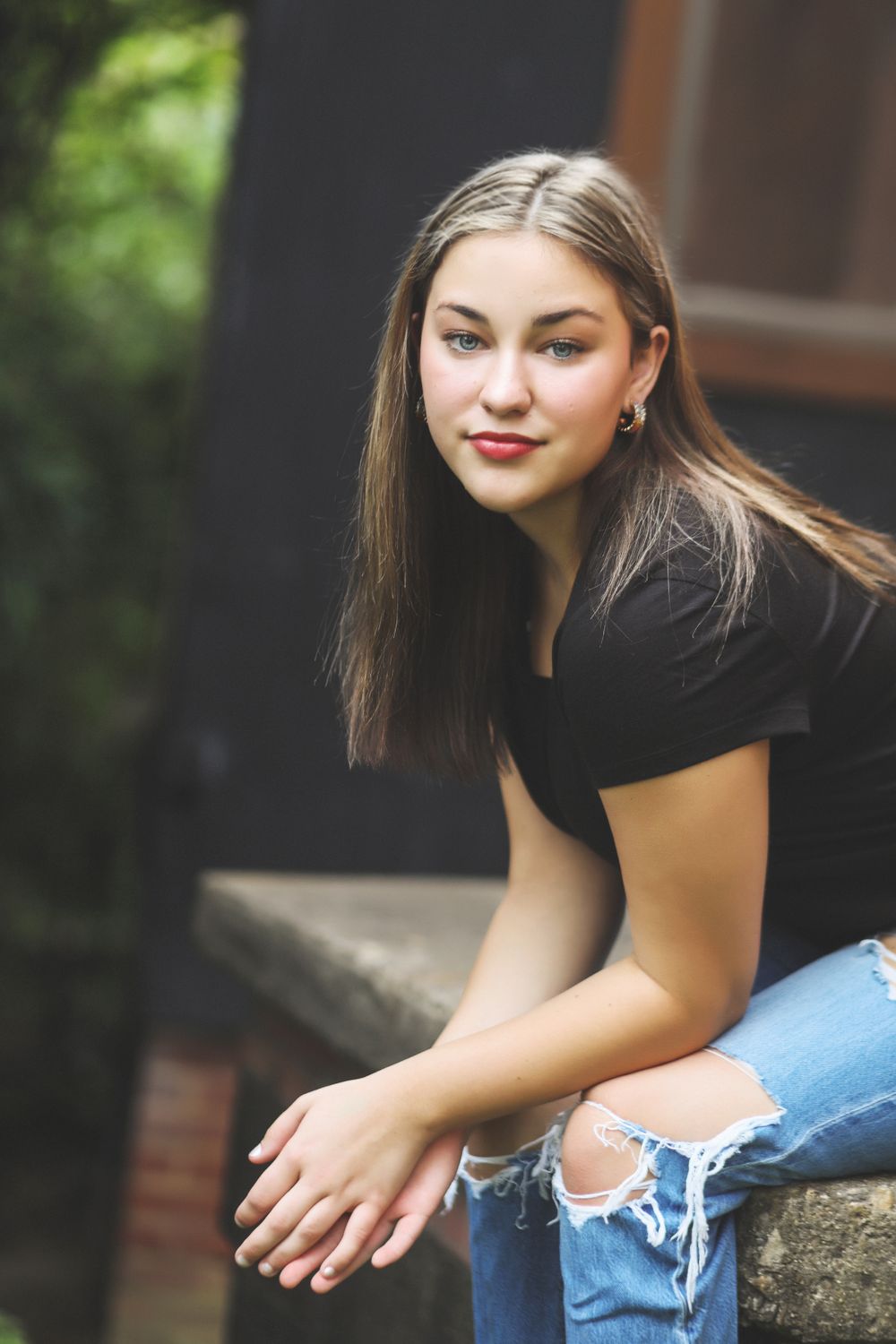 Casual portrait wearing ripped jeans and black top while sitting outdoors.