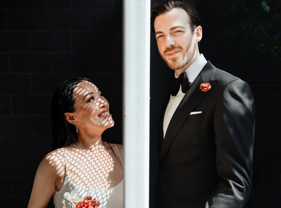 Wedding couple posing against a dark background with dramatic lighting.