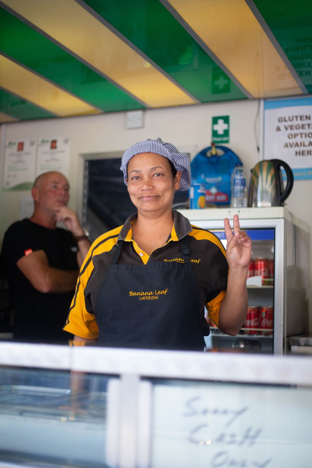 Food service worker in yellow uniform and cap making peace sign while working at counter.