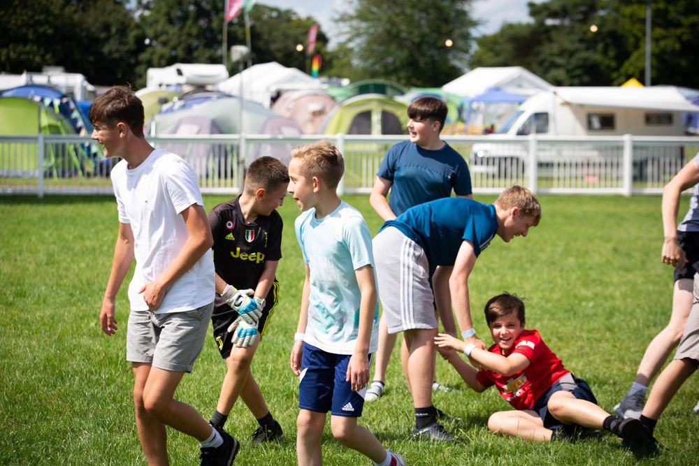 People playing outdoor games on a grassy field with tents in the background.
