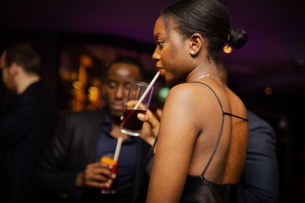 Person in formal attire enjoying a drink at a dimly lit social event.