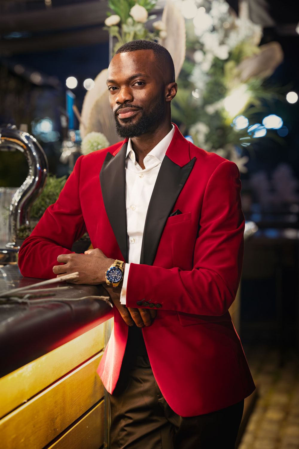 A stylish red blazer creates an elegant contrast against the dark bar interior with floral decorations.