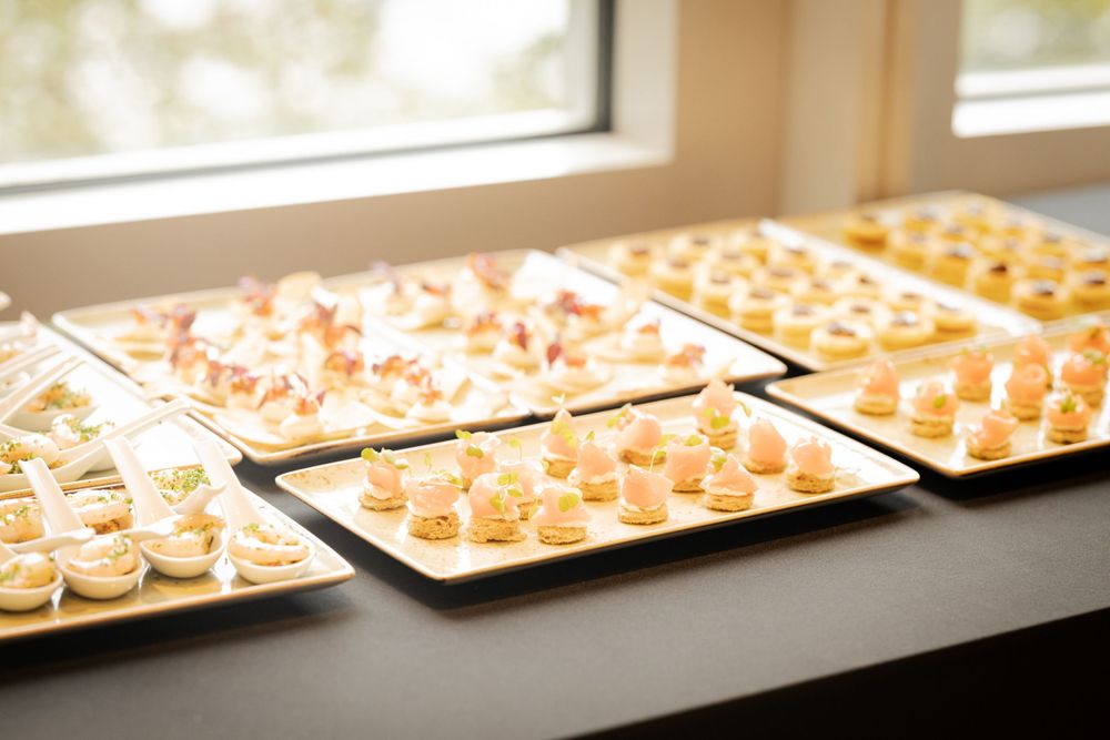 Multiple trays of elegant appetizers and hors d'oeuvres displayed on white plates near a window.