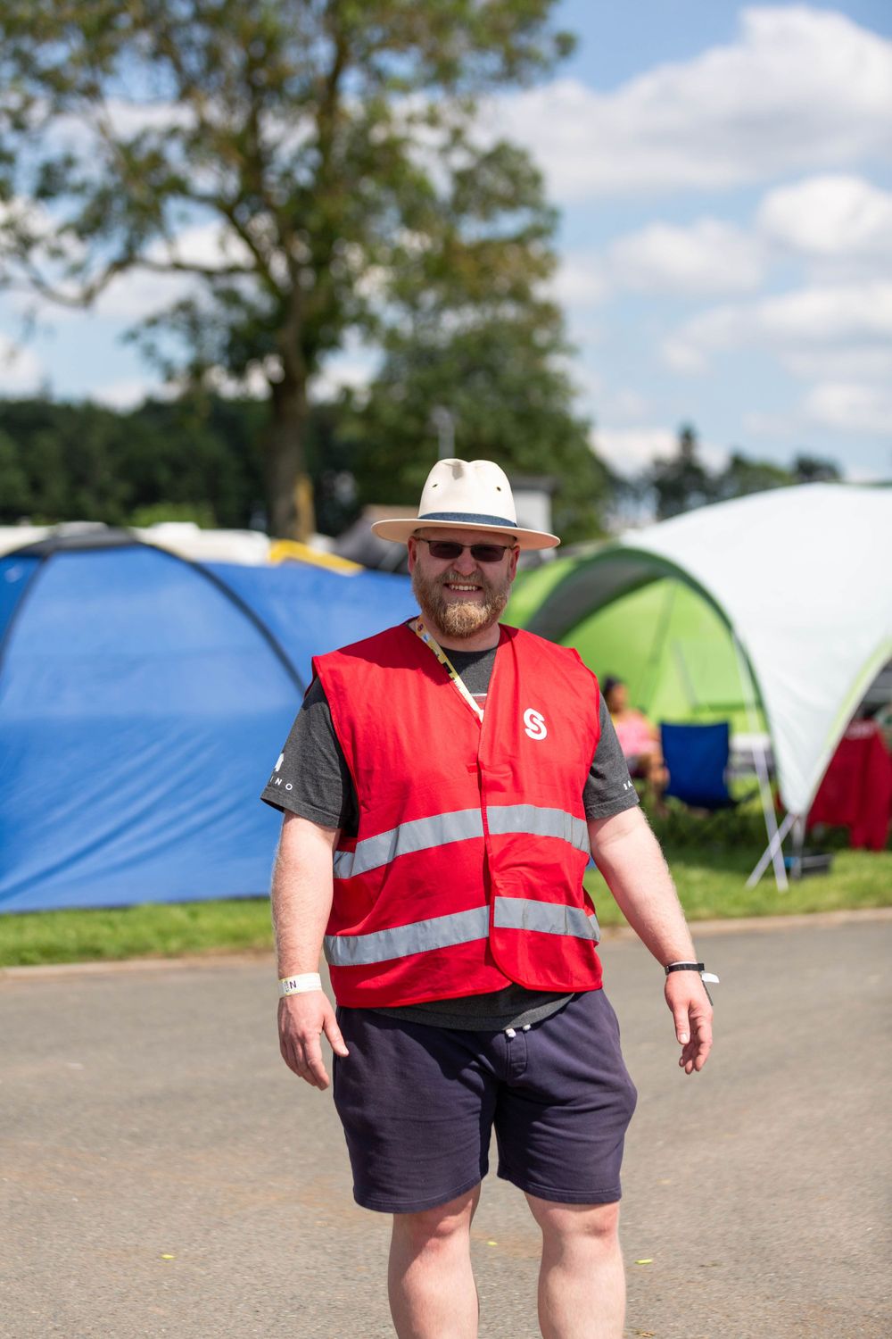 A volunteer in a high-visibility vest standing near camping tents on a sunny day.