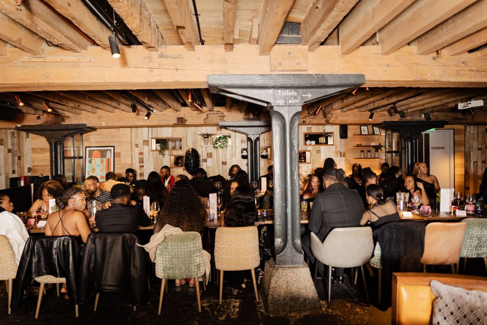 A full restaurant dining room with exposed wooden beams and industrial decor hosting evening dinner service.