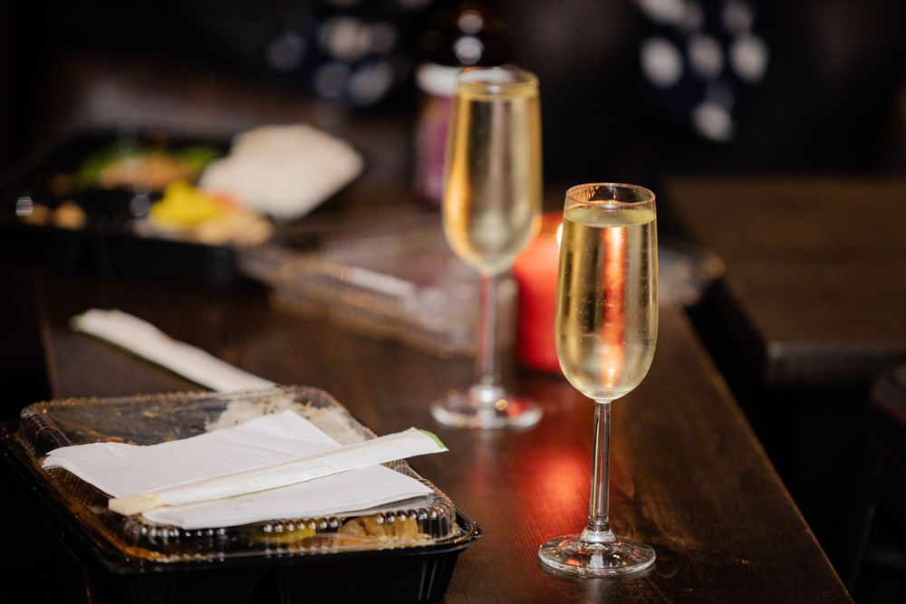 Two glasses of champagne sit on a wooden table next to papers in a dimly lit setting.