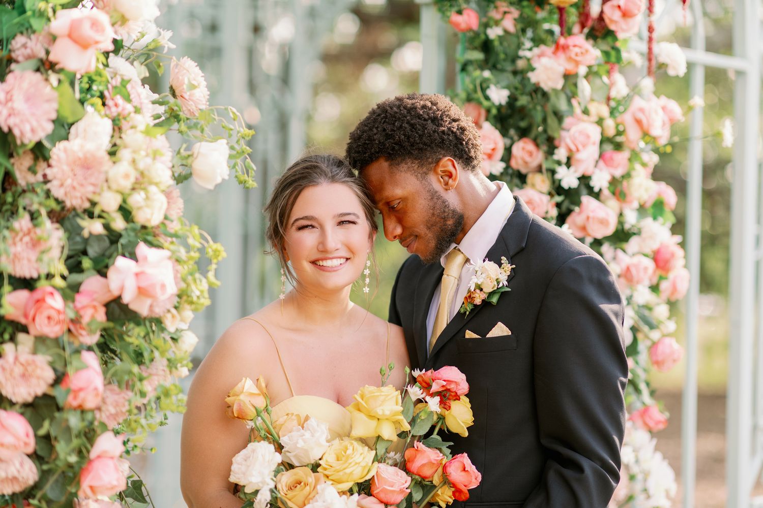 Wedding couple shares intimate moment under arch of pink and white roses.
