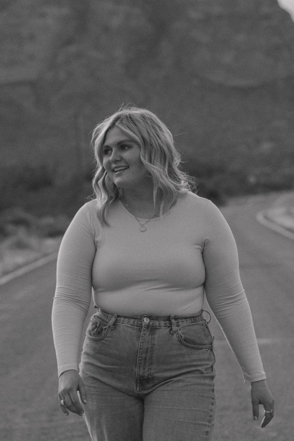 A casual outdoor portrait in black and white against a mountainous backdrop.