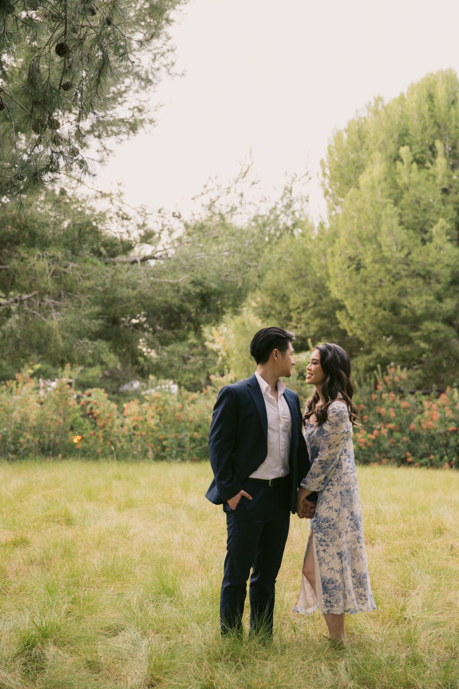 Couple in formal wear sharing romantic moments in a green meadow with trees.