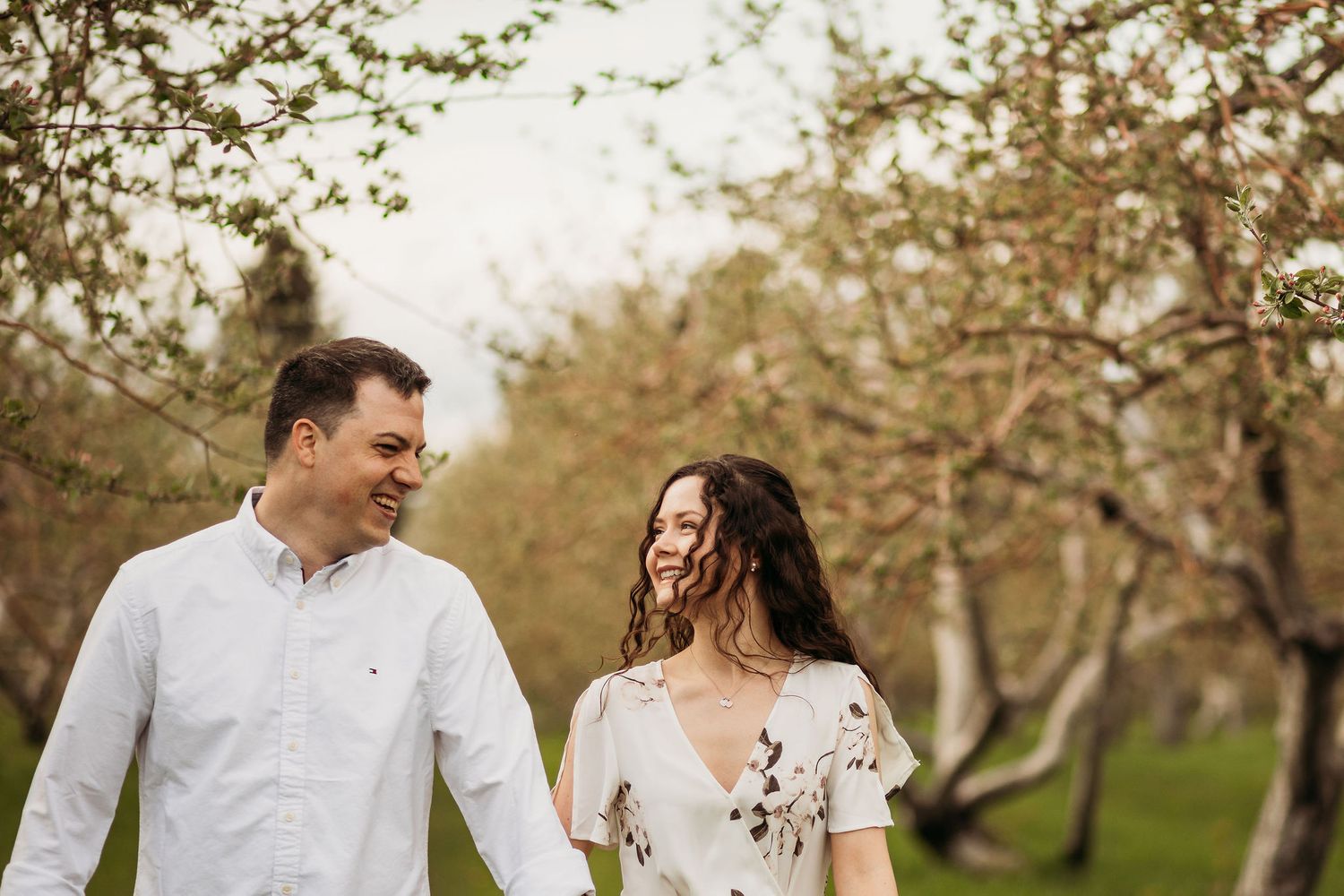 A couple walks together smiling in a spring orchard with blooming trees.